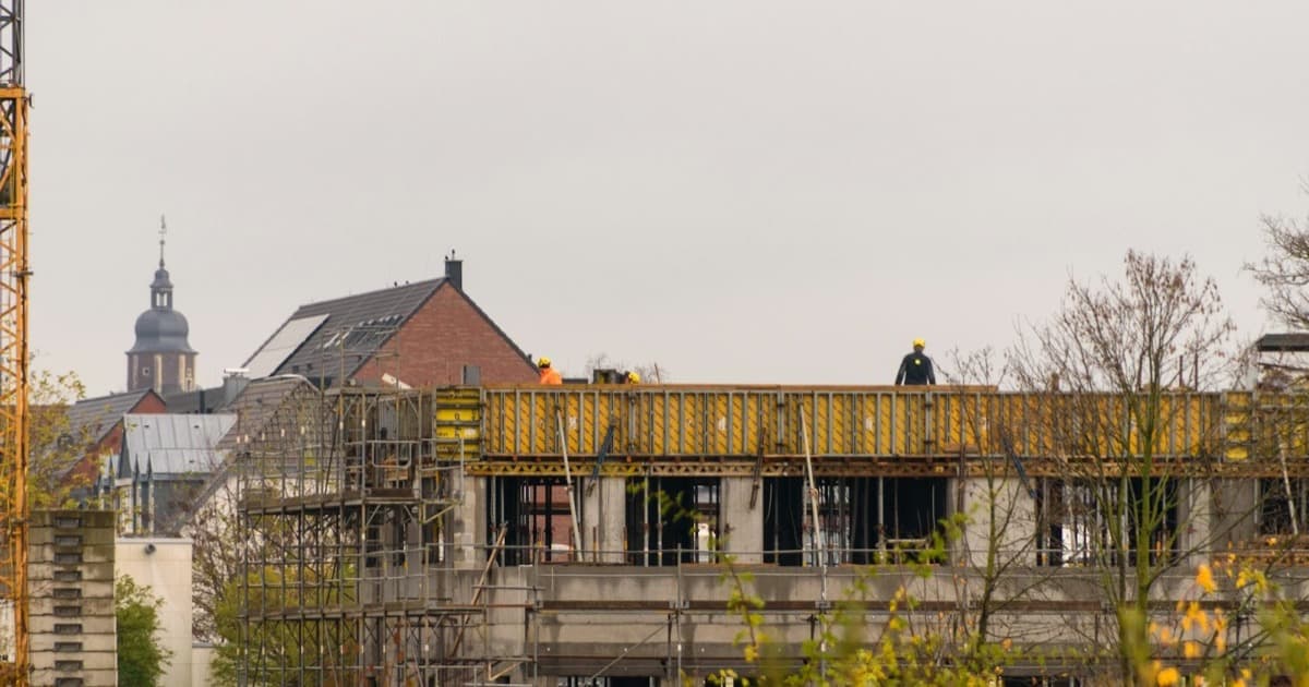 Construction workers on a partly-built concrete structure on an active site beneath an overcast sky.