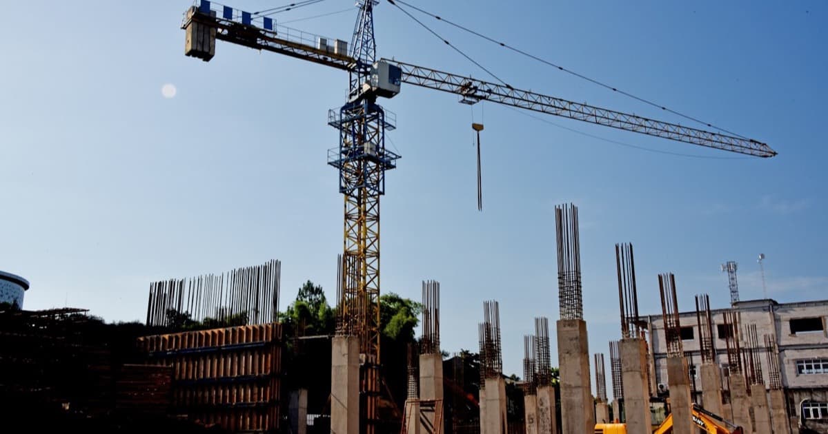 An early-stage construction site with reinforced-concrete columns rising beside a tower crane under a clear sky.