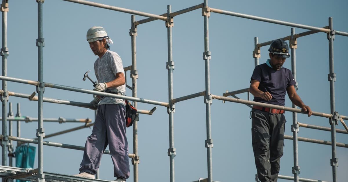 Two construction workers in hard hats working at height on metal scaffolding.