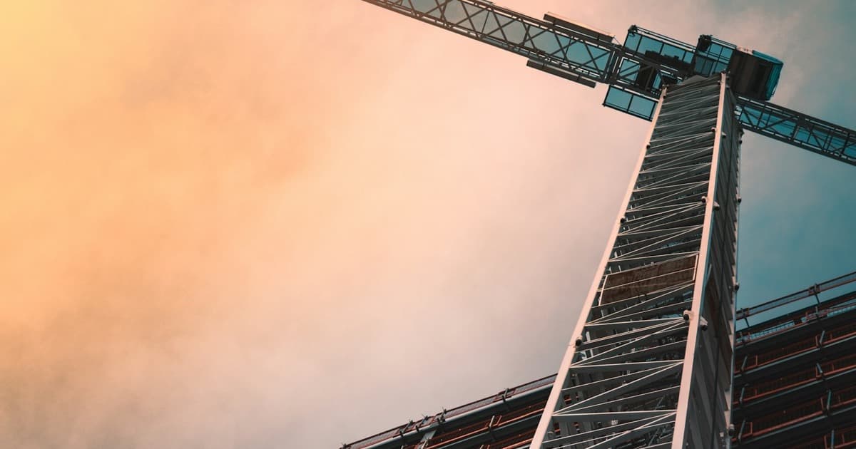 A low-angle view of a tower crane against a warm sky above a building under construction.
