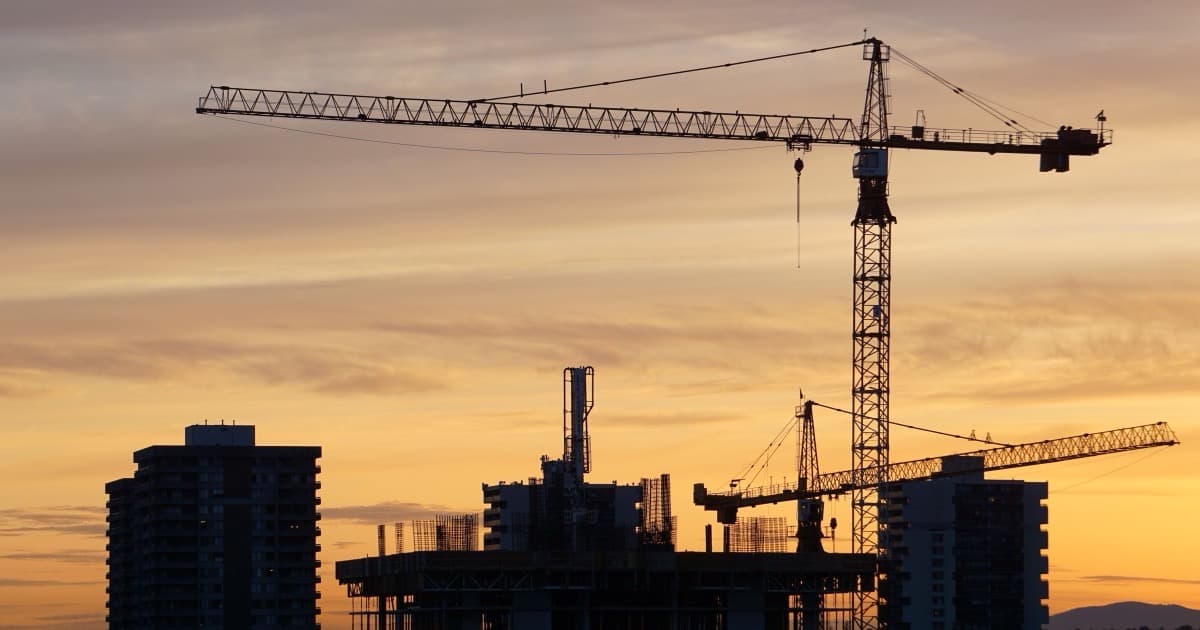 Silhouette of tower cranes and buildings against a sunset city skyline.