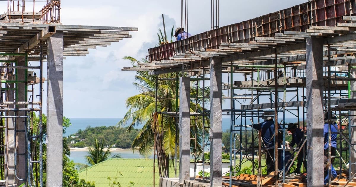 Workers building a reinforced-concrete structure with scaffolding on a coastal construction site.