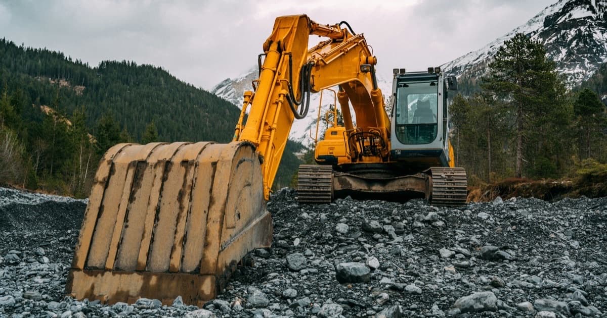 A tracked excavator standing on rocky ground in a mountain valley.